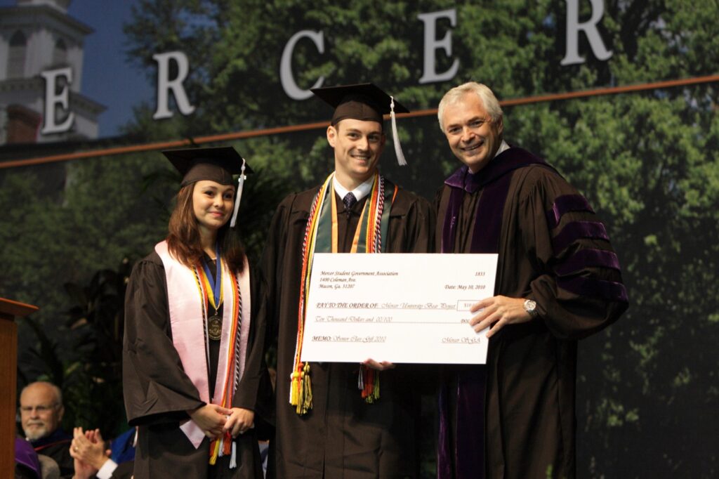President Underwood standing with a couple of recent graduates, holding a ceremonial check